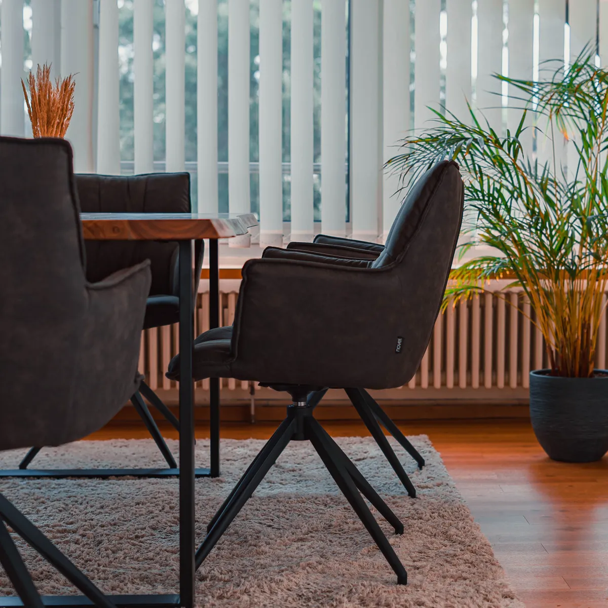 A conference table ringed by upholstered swivel chairs in a quiet, daylit meeting room, with a potted palm beside the window.